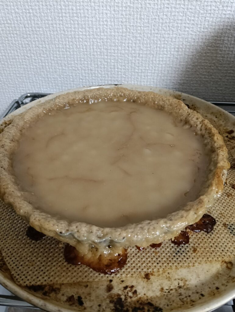 アレルゲンフリーチーズフィリングを流しいれたタルト台を焼いたもの。タルト台の縁にフィリングがはみ出し、凝固している。
